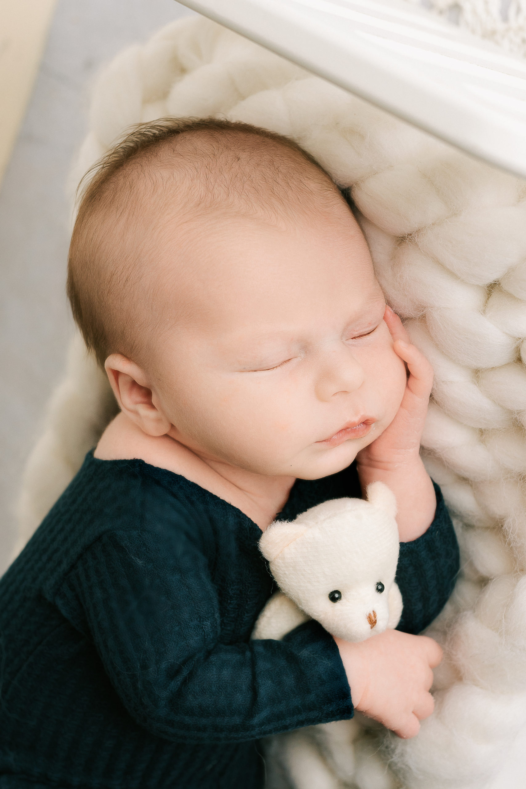 newborn baby boy sleeping with a teddy bear on a white bed