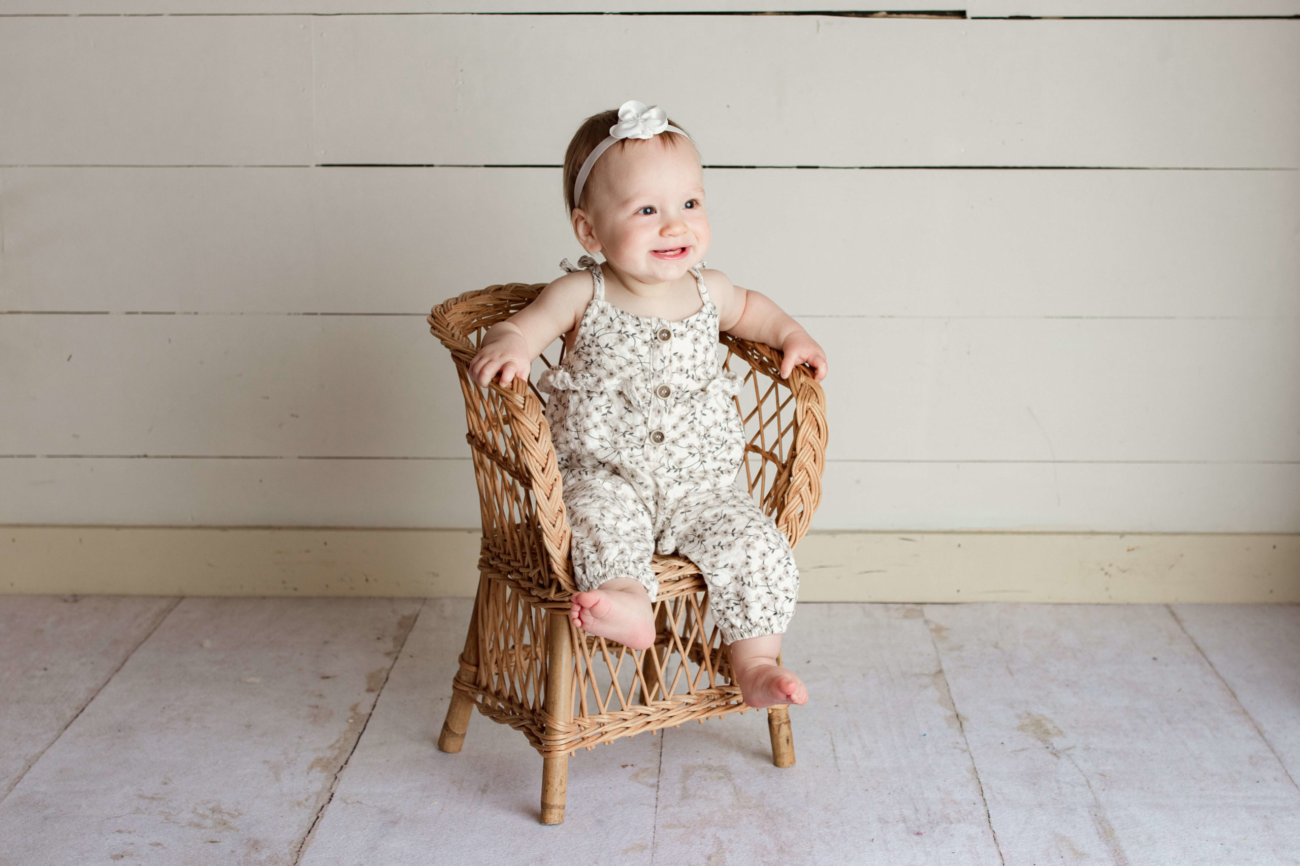 9 month old baby girl sitting in a wicker chair wearing a floral jumper