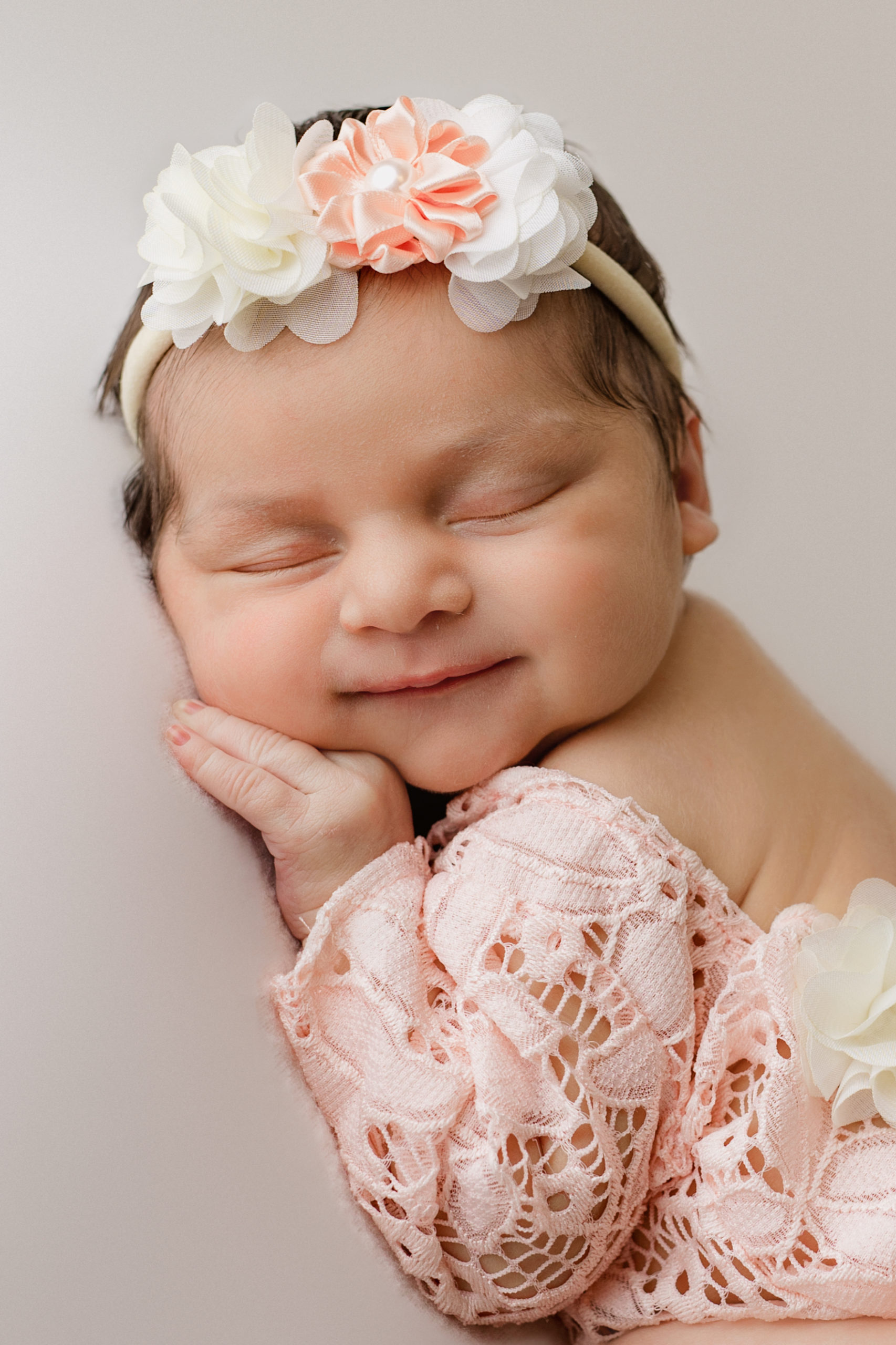 newborn baby girl smiling with her hand under her chin with a photo done by Milwaukee newborn photographer