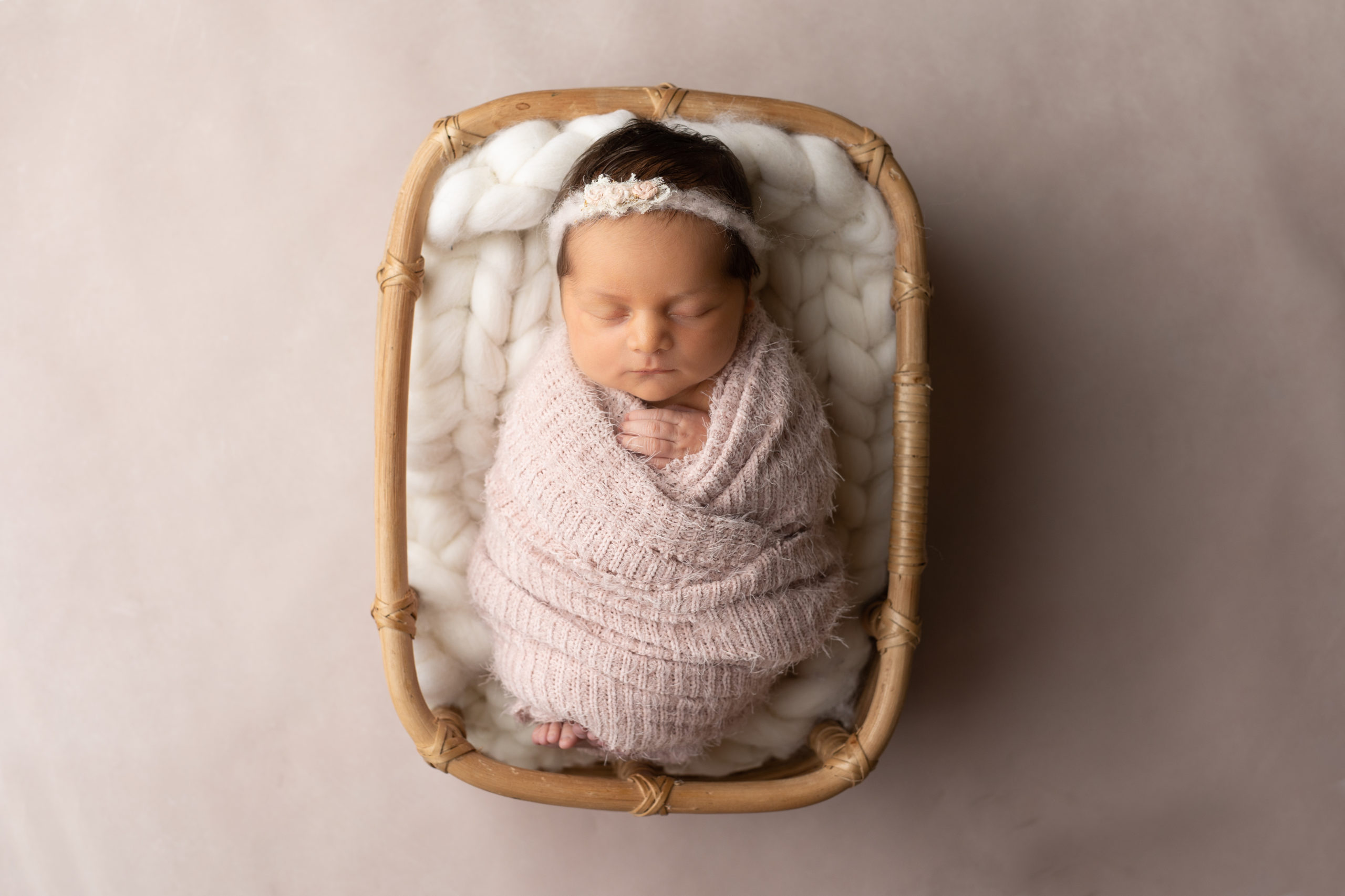 newborn baby girl in a tan basket with pink background in a light pink blanket in Milwaukee