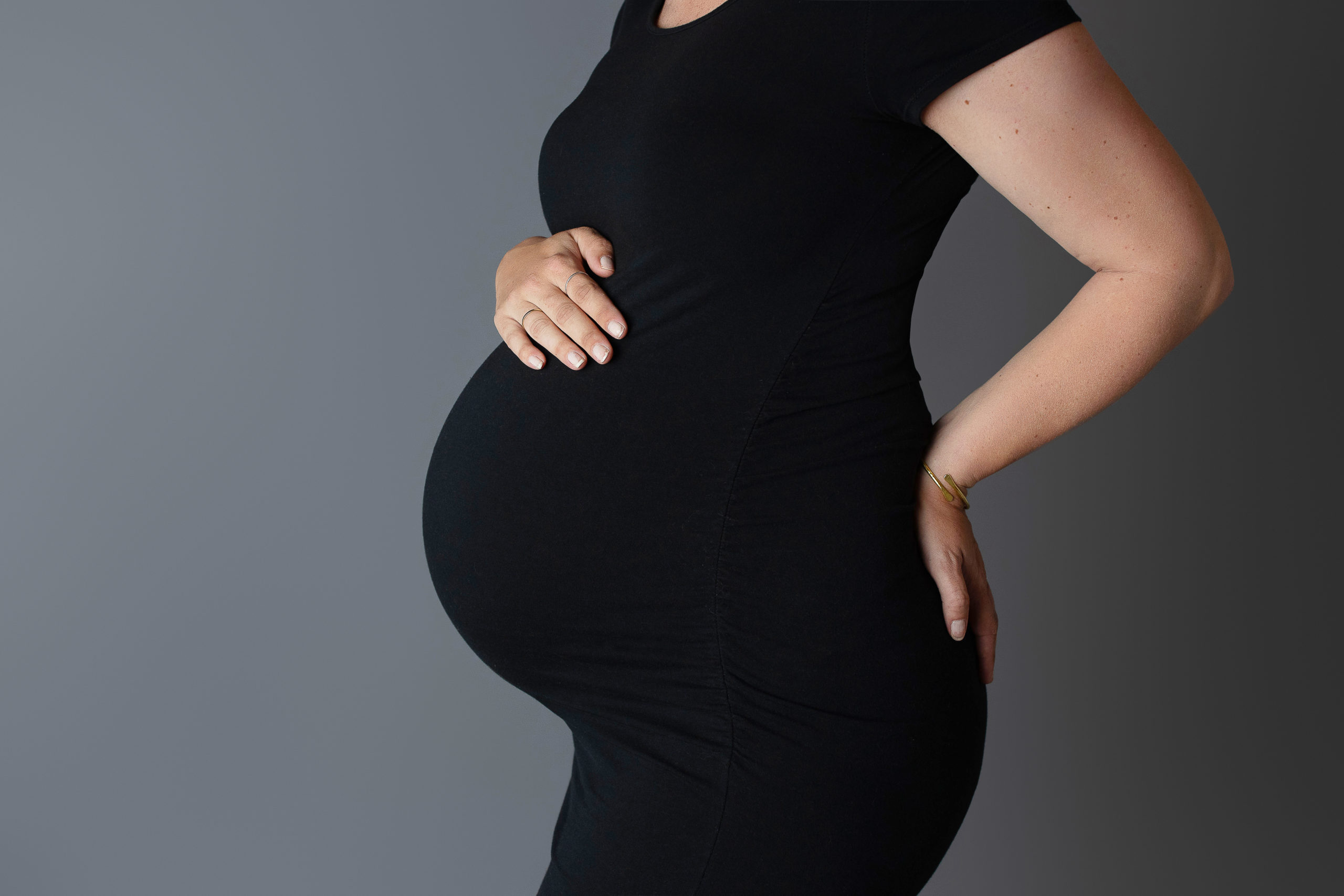expectant mother wearing black dress with her hand on top of her belly while getting photographed by Milwaukee area maternity photographer