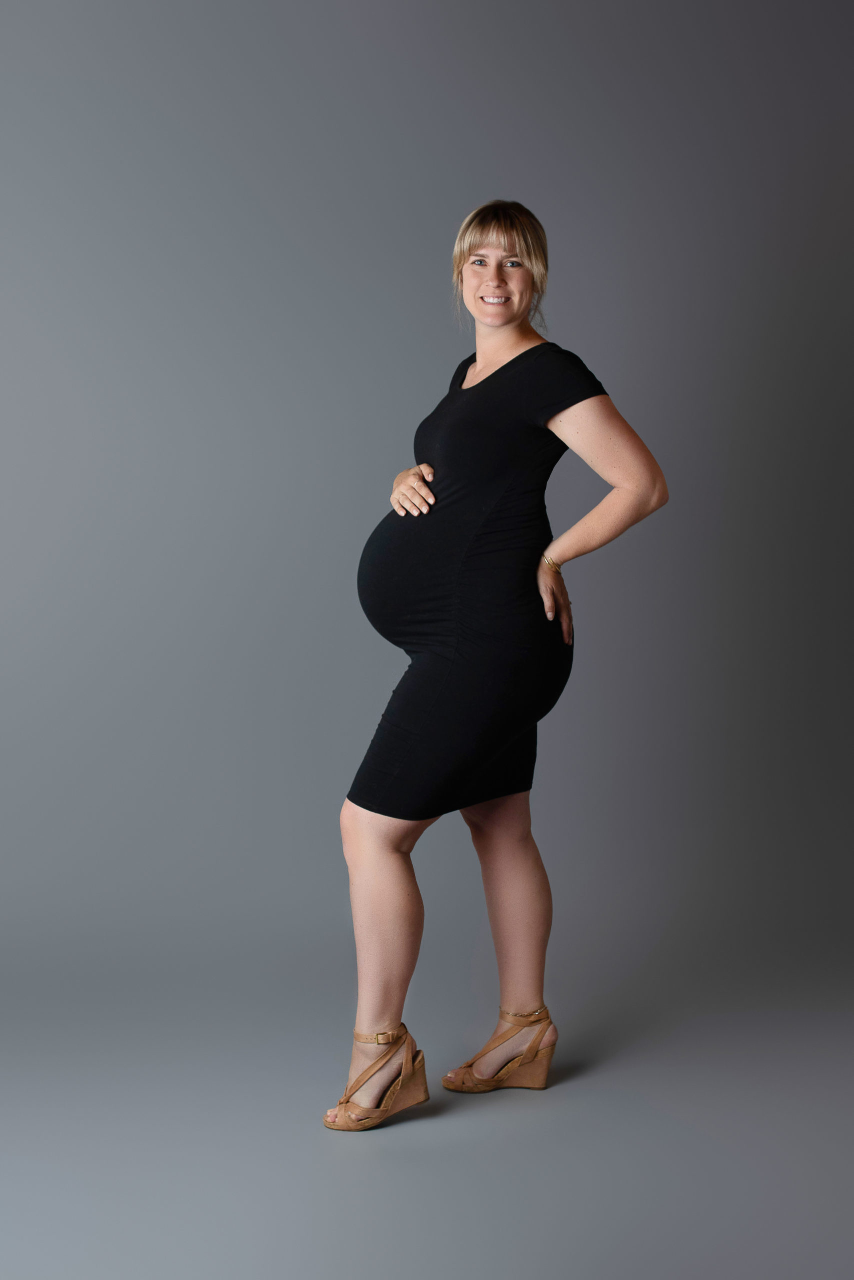 expectant mother wearing a black dress while getting maternity pictures in Milwaukee studio