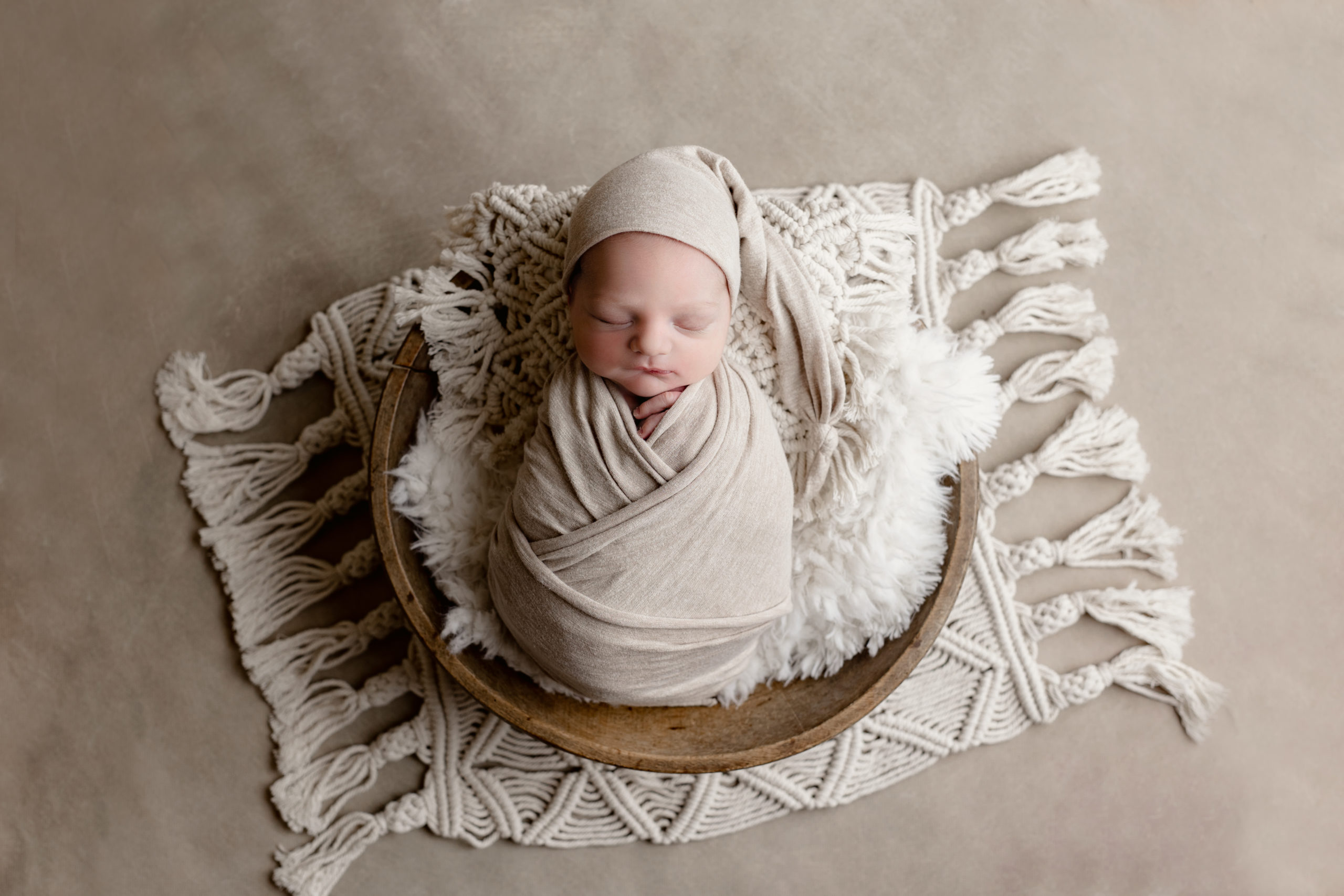 newborn baby boy in a brown bowl with a tan wrap around him in pictures with a Milwaukee newborn photographer