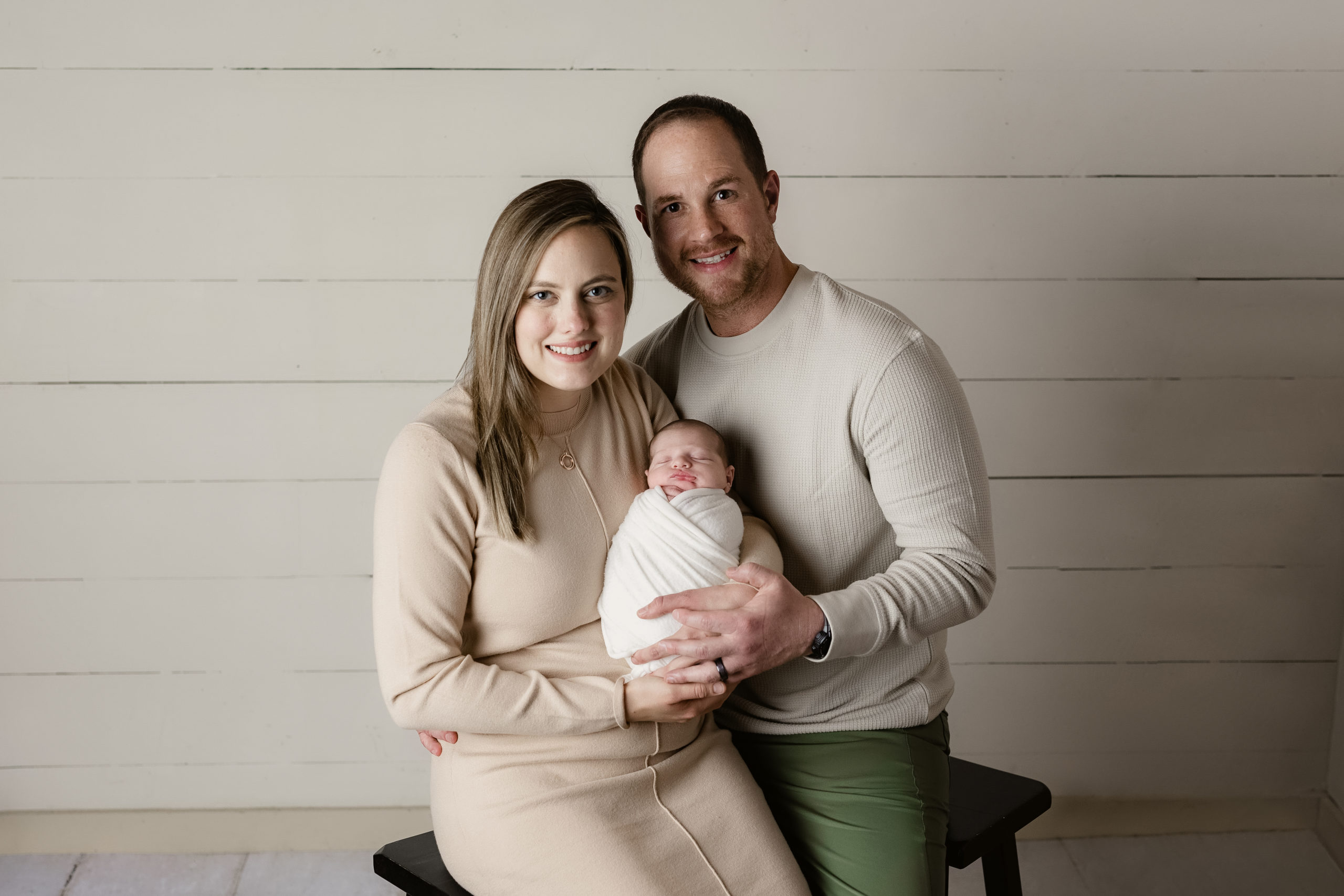 newborn baby boy being held by mom and dad wearing cream colored outfits for photos with a Milwaukee newborn photographer