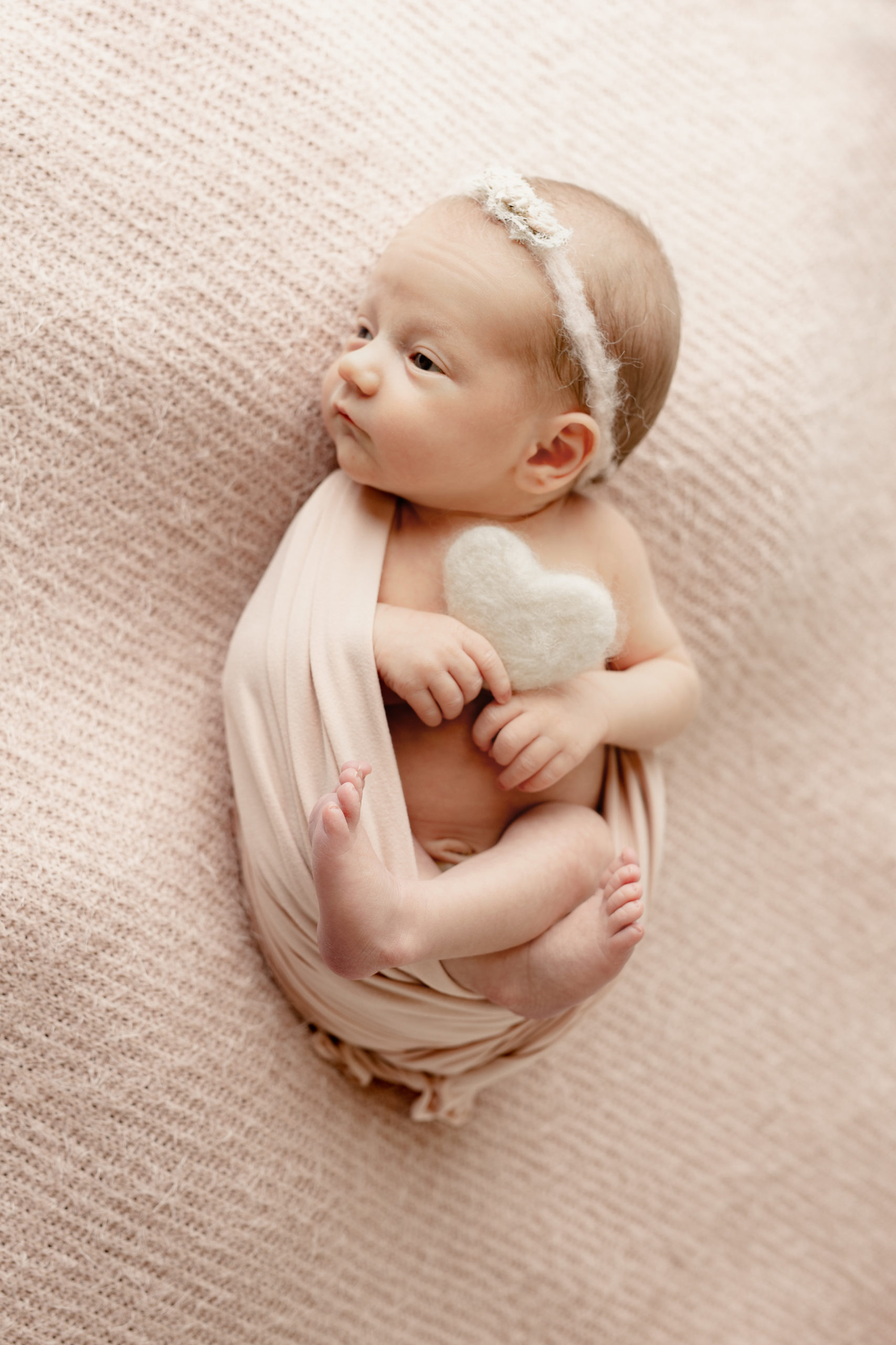 Newborn girl holding onto a white felt heart while getting newborn pictures in Milwaukee