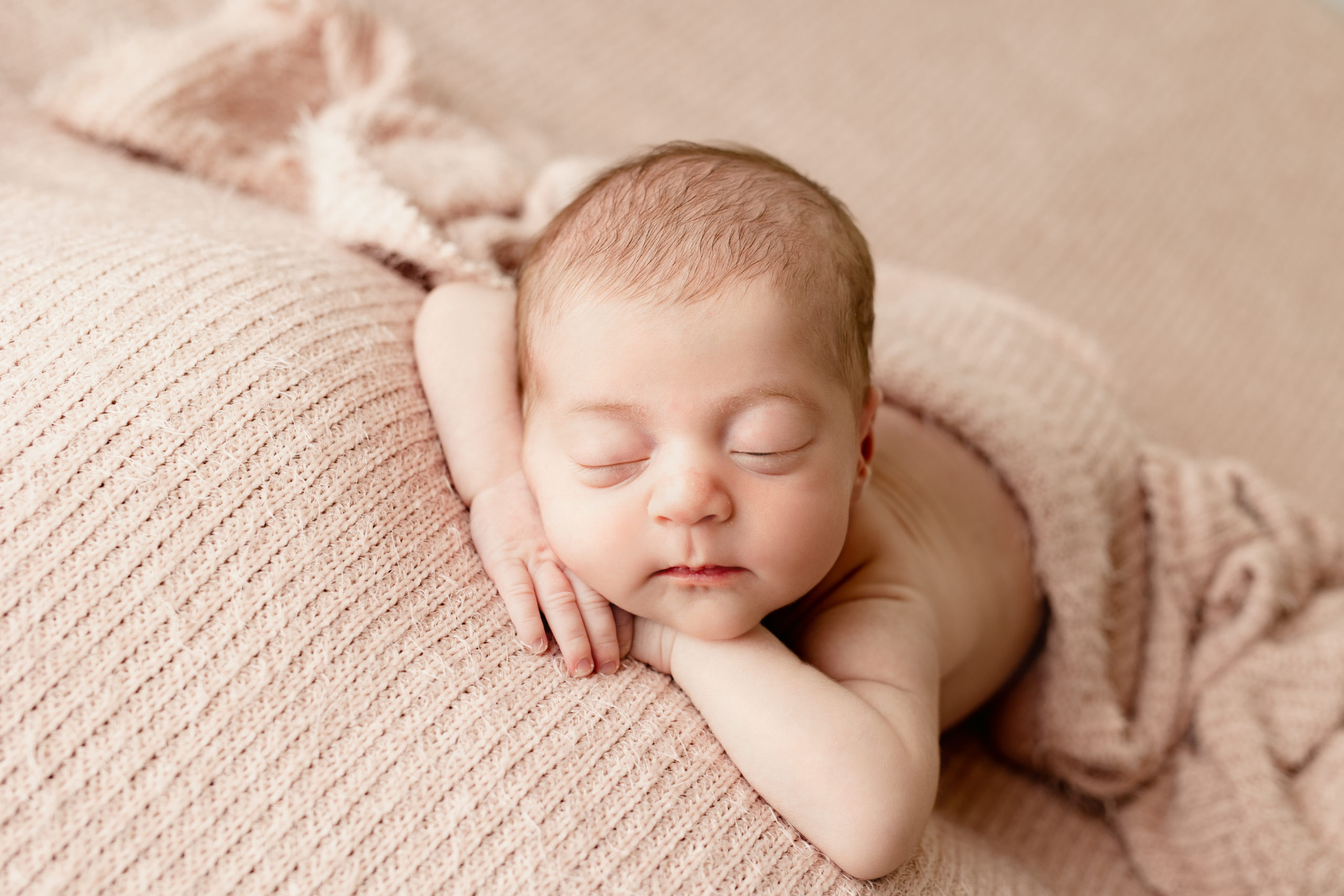newborn baby sleeping on her arms with a pink blanket