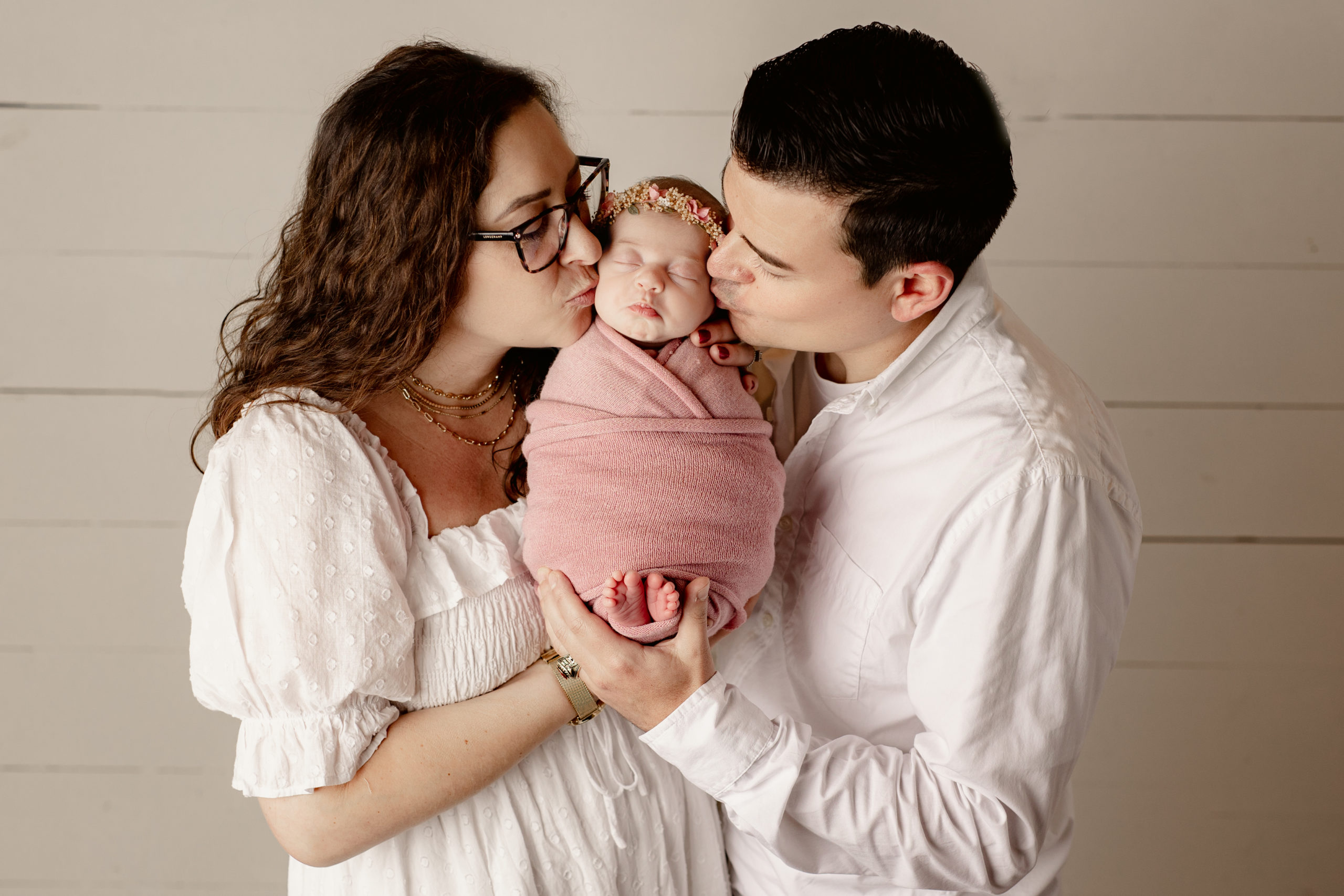 new mom and dad holding their newborn baby girl in pink and kissing her cheeks Milwaukee Fertility Clinic