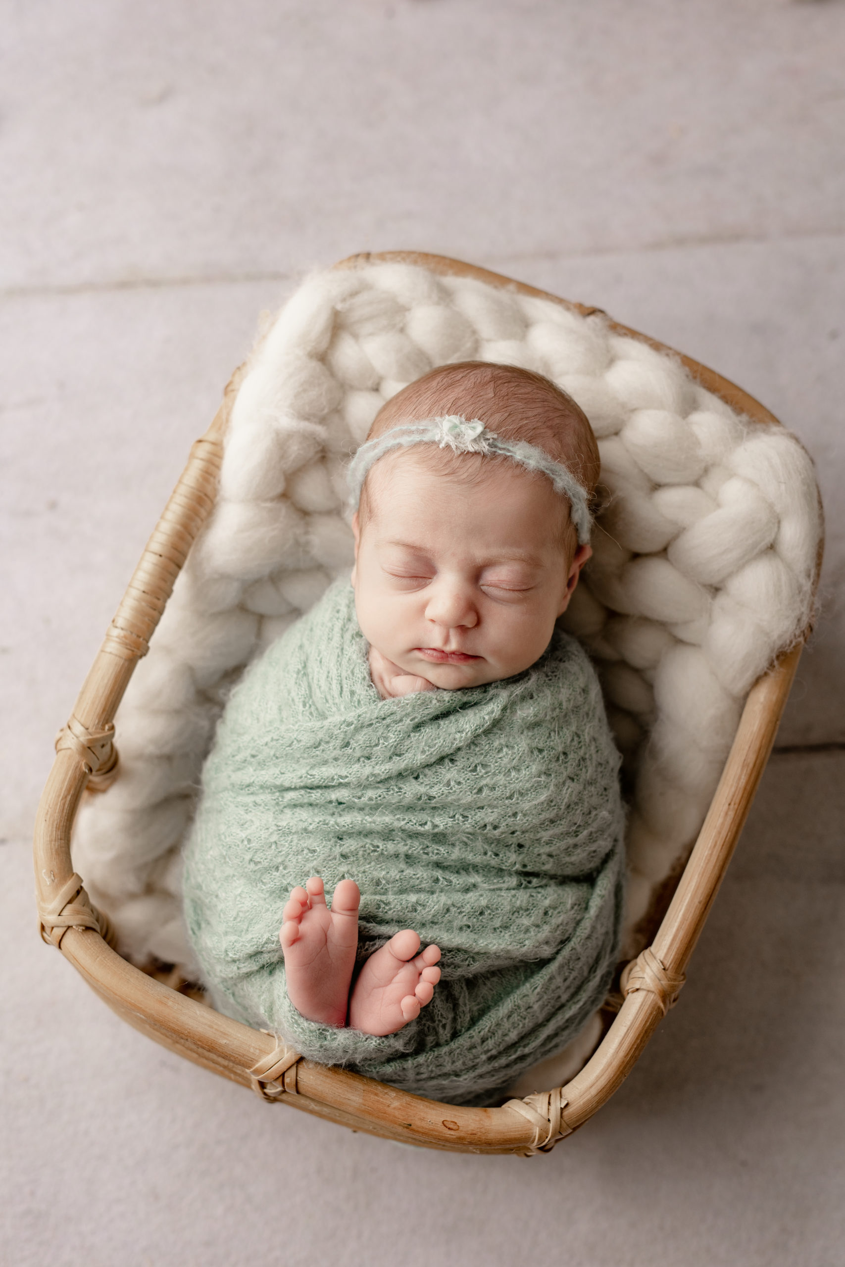 newborn baby girl wrapped in green, sleeping in a basket