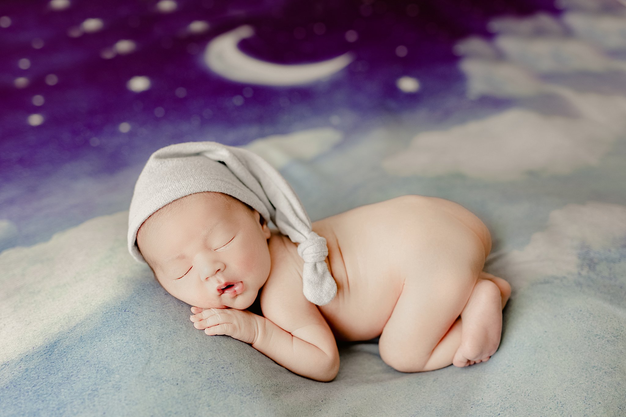 newborn baby lays on night sky blanket wearing only a night cap