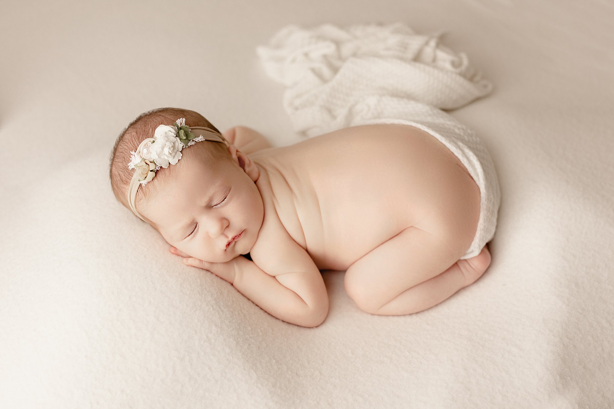 newborn baby laying on a cream blanket with a floral headband