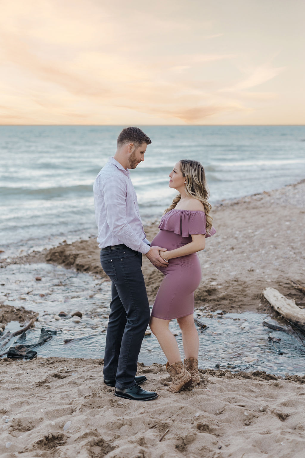 A happy couple stand on a beach while holding the pregnancy bump at sunset after getting 3d ultrasound milwaukee