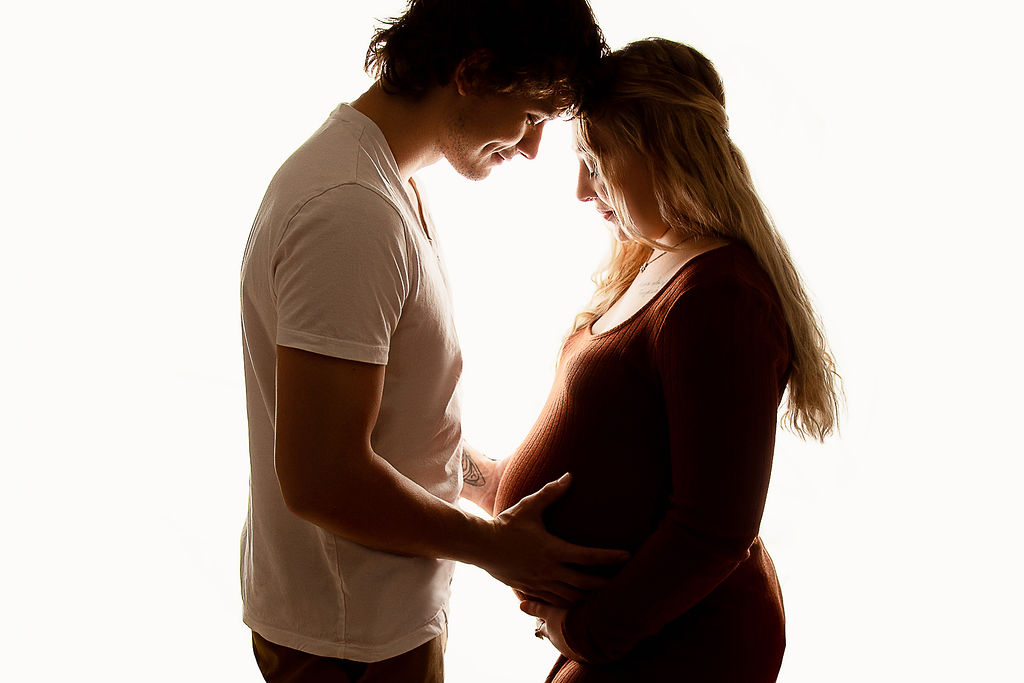 Expecting parents smile while touching foreheads and holding the bump in a studio after visiting aurora birthing center