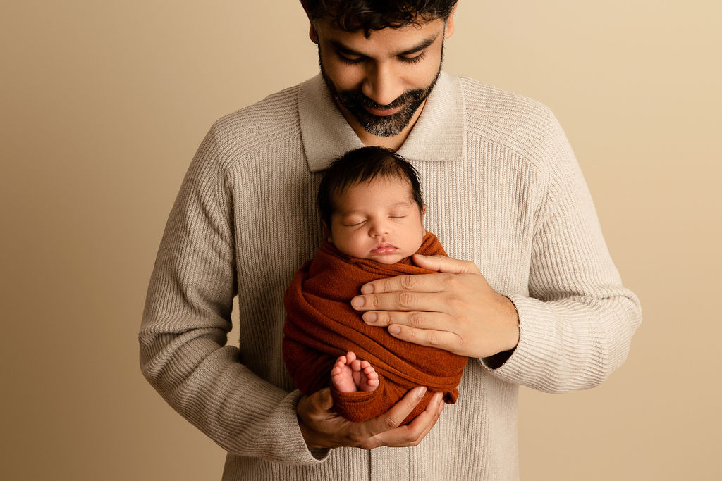 A happy father cradles his sleeping newborn baby against his chest while standing in a studio after using car seat installation milwaukee