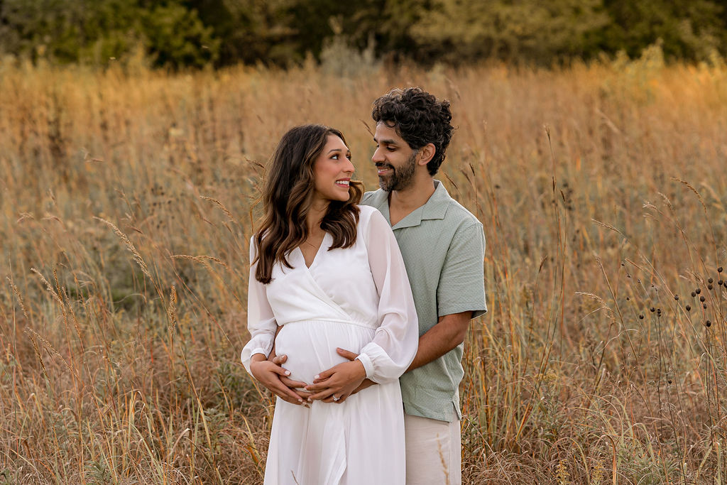 Happy expecting parents hold the bump while hugging and standing in a field at sunset after meeting doula waukesha wi