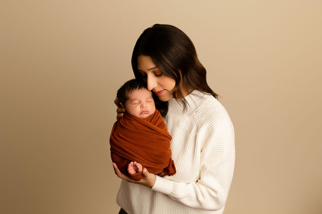 A new mother in a white sweater stands in a studio snuggling her sleeping newborn baby after visiting float milwaukee