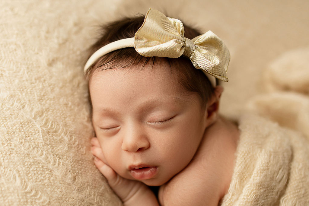 A newborn baby girl sleeps on a cream bed in a gold bow after meeting germantown pediatricians