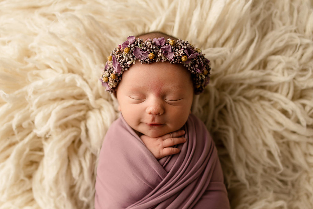 A newborn baby sleeps in a purple swaddle and matching headband before some infant swim lessons milwaukee