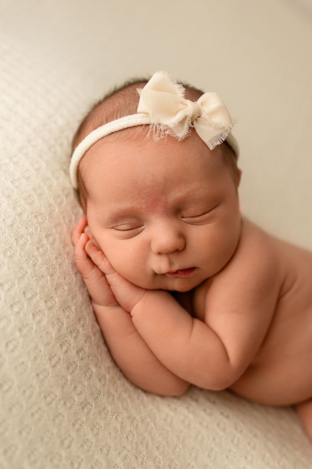 A newborn baby sleeps on her hands in a white bow thanks to lactation consultant milwaukee