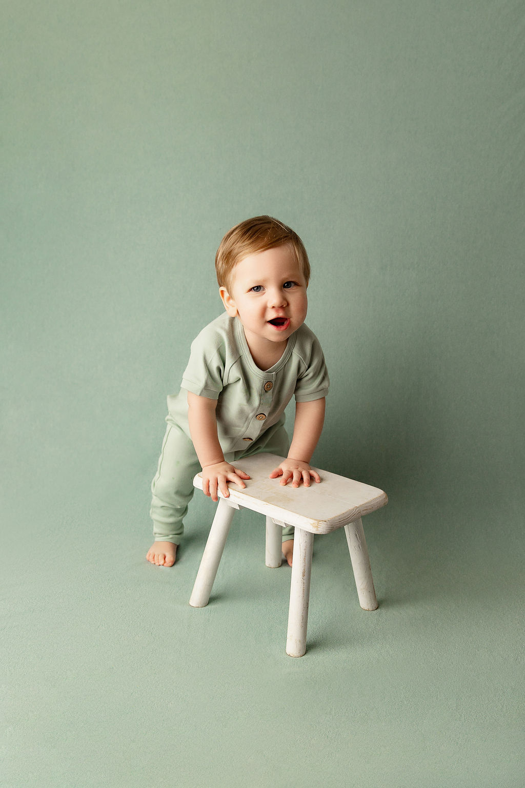 A toddler boy smiles while playing with a small wooden stool in a green onesie after visiting milwaukee daycare