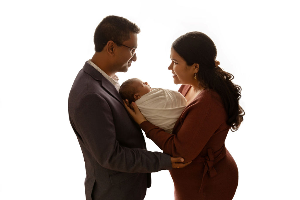 Happy parents stand in a studio cradling their sleeping newborn baby between them thanks to milwaukee fertility clinic