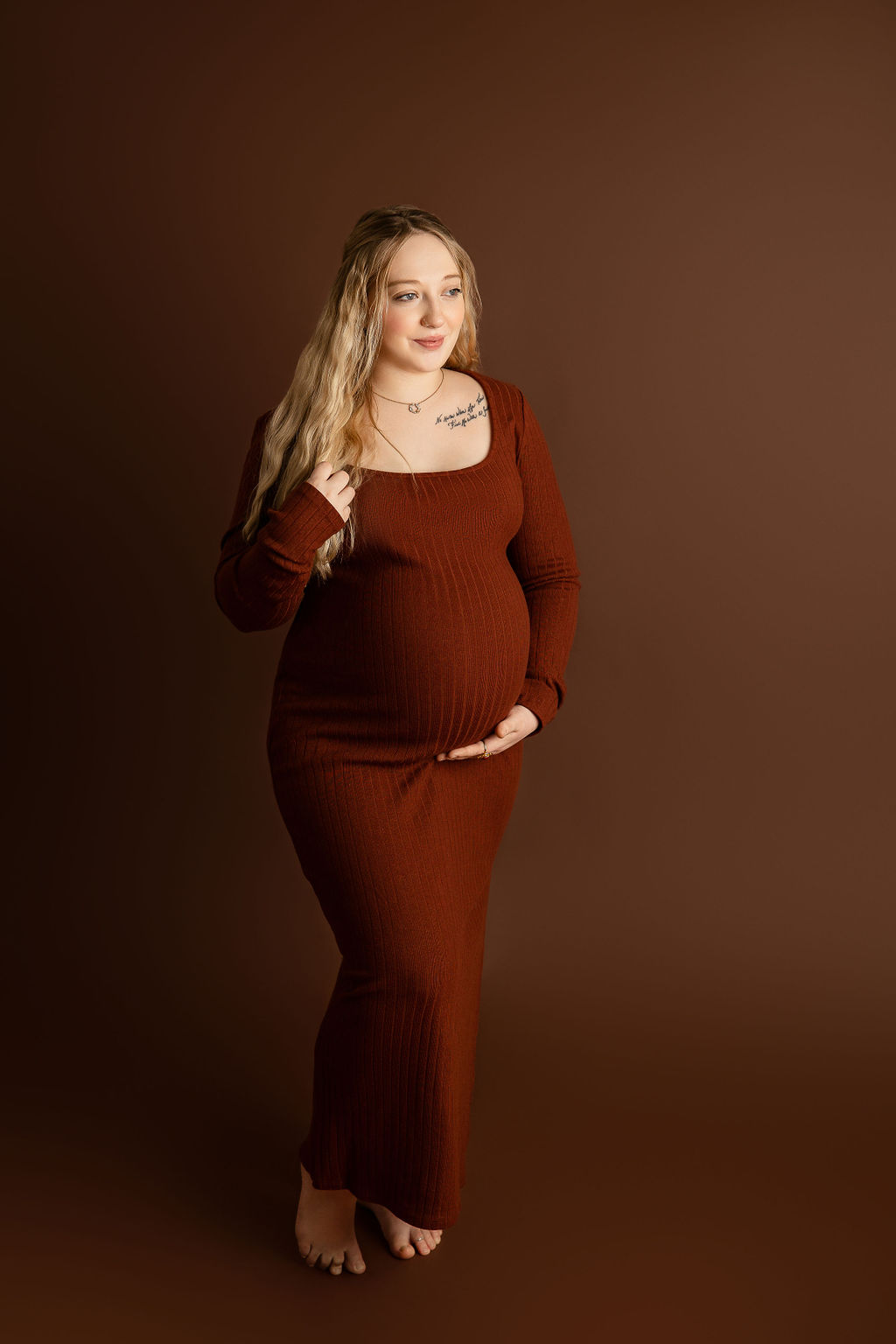 A mom to be stands in a studio in a red maternity gown holding her bump and hair after meeting milwaukee midwife