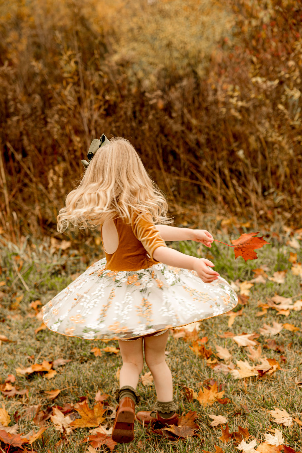 A toddler girl in a dress twirls and dances in a park in fall before visiting milwaukee toy stores