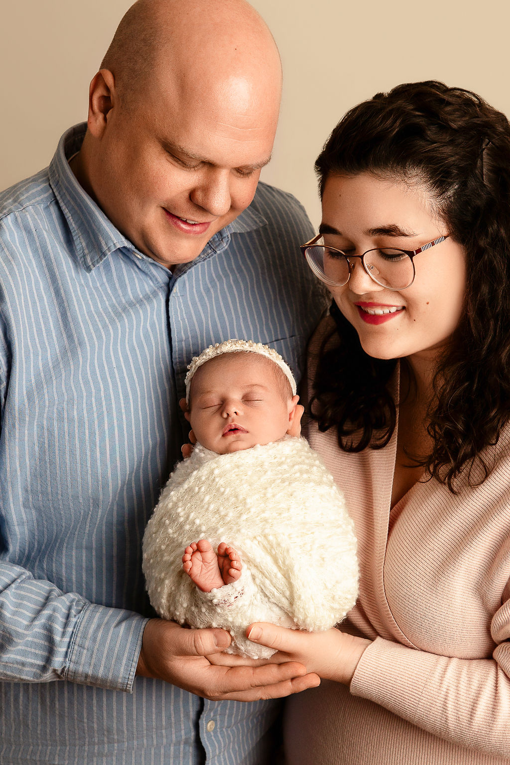 Happy parents hold their sleeping newborn baby in their hands while standing in a studio thanks to postpartum doula milwaukee
