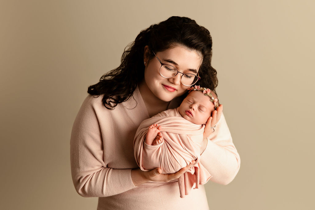 A new mother cradles her sleeping newborn baby while standing in a studio before meeting a postpartum doula milwaukee