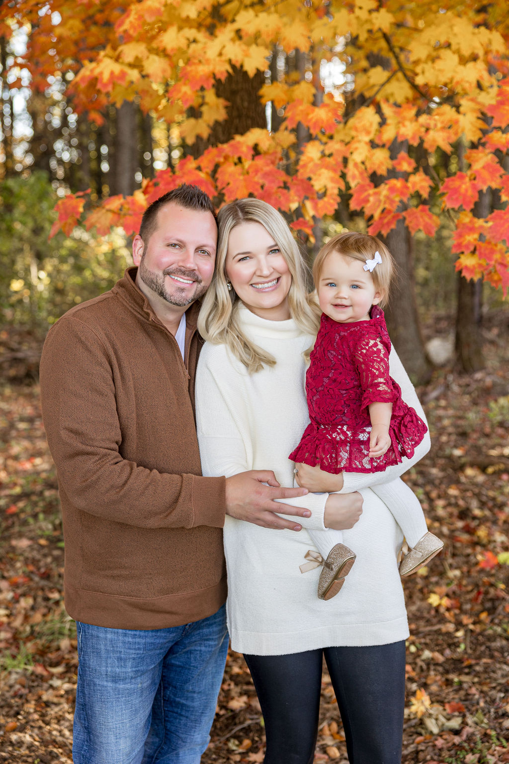 Happy parents stand in a park in fall with their toddler daughter