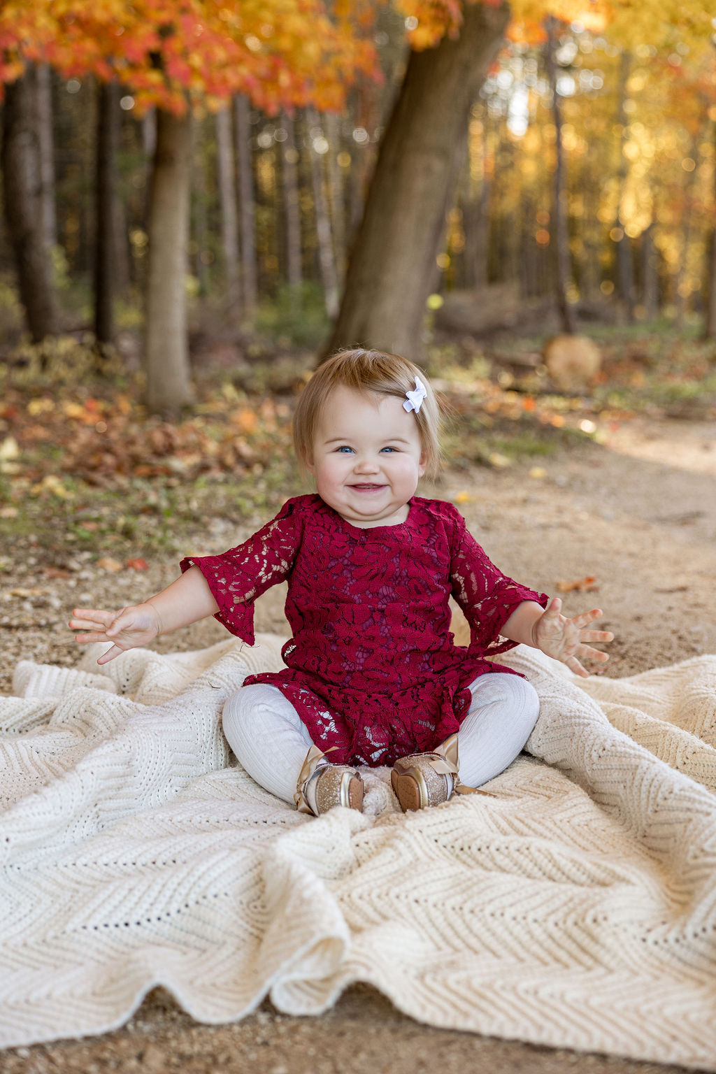 A happy toddler in a red dress sits on a picnic blanket in a park trail in fall after visiting shorewood family chiropractic