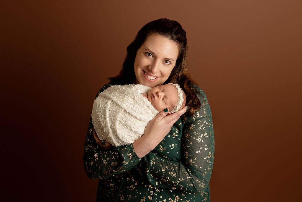 A happy mother cradles her sleeping newborn baby while standing in a studio thanks to waukesha obgyn