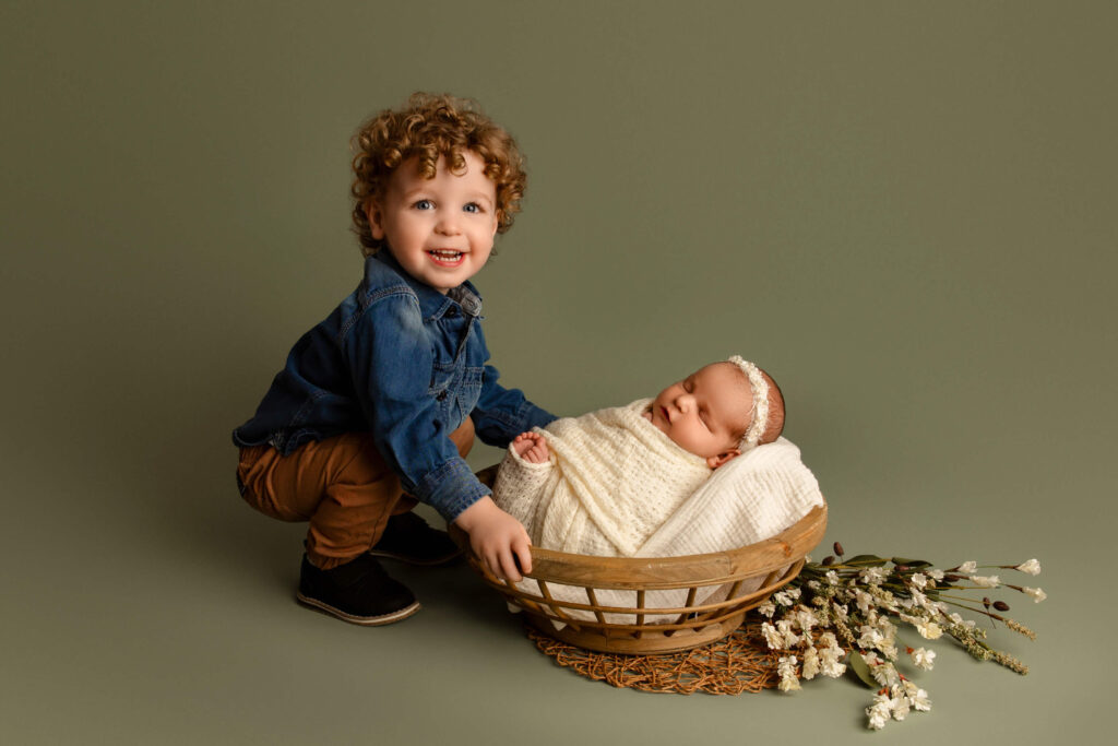 Toddler baby holding onto his new baby sister in a wooden bowl during newborn photos in Brookfield, WI

