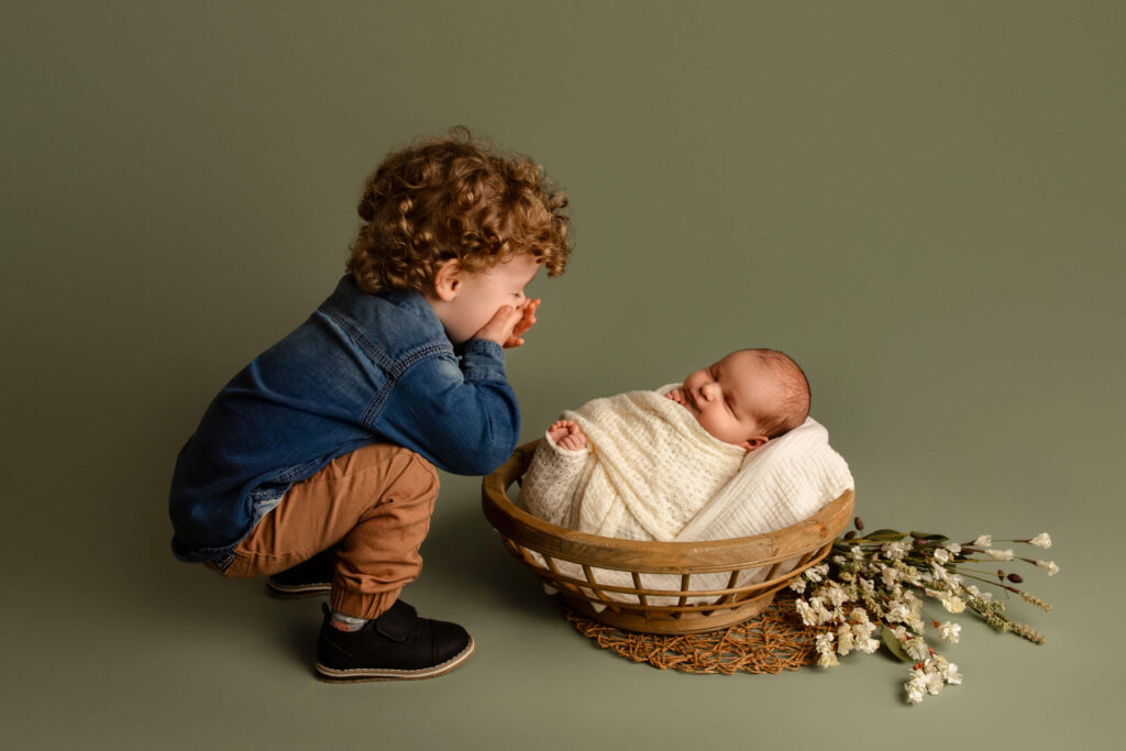 Big brother laughing as he looks at his baby sister during newborn photos
