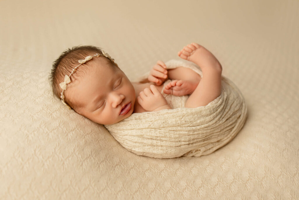 Newborn baby in the womb pose on a cream backdrop and bow headband